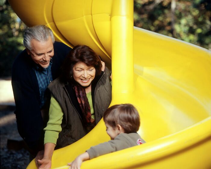 Elderly couple smiling and watching child on yellow slide, illustrating family dynamics and golden child stories.