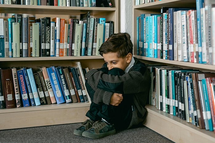 Sad young boy sitting alone in a library corner, illustrating estranged parents and family neglect after 20 years.