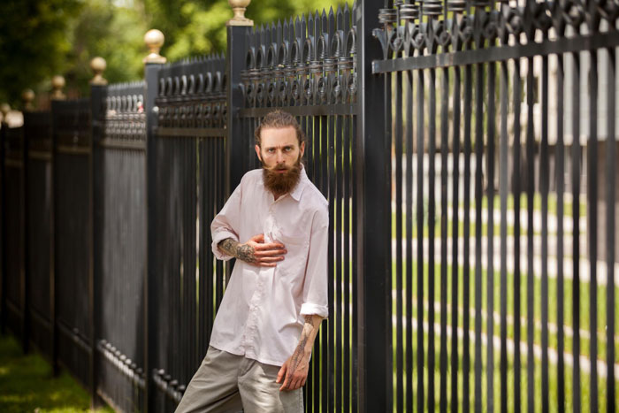 Man with tattoos and beard standing by a new black iron fence after neighbor replaced rotten fence without agreement