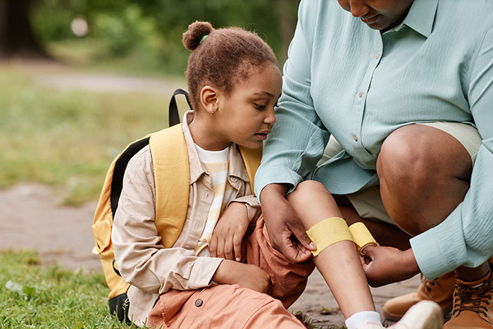Child with backpack receiving first aid on injured leg outside, highlighting kids using neighbor&rsquo;s yard without asking incident.