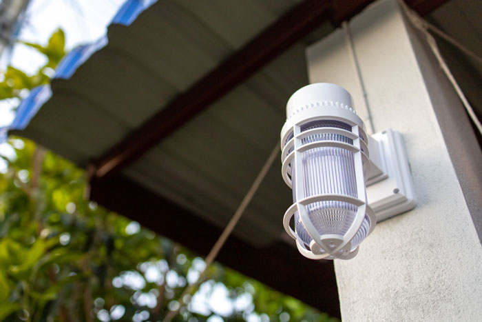 Outdoor solar light installed on a house exterior with trees in the background during daylight sunlight.