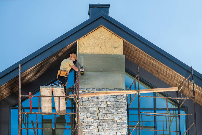 Construction worker installing stone facade on a modern house chimney under neighbours installed actual sun lighting outdoors.
