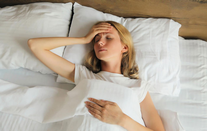Woman resting in bed with eyes closed and hand on forehead, illustrating effects of neighbours installed actual sun exposure.