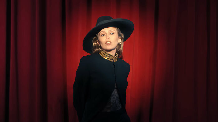 Person posing in front of red curtains wearing a black hat and jacket, symbolizing nepo babies insider experiences.