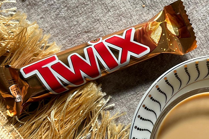 Twix candy bar wrapped in gold packaging next to a cup of coffee, illustrating gas station workers wild stories.