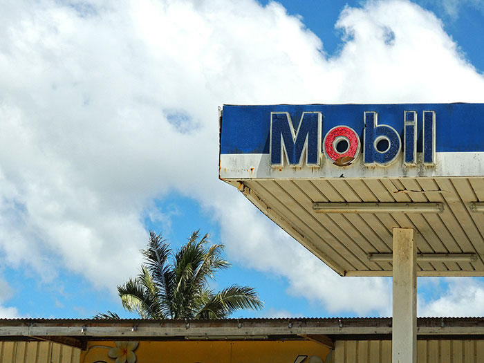 Old Mobil gas station canopy with blue sky and palm trees, representing gas station workers and their wildest stories.