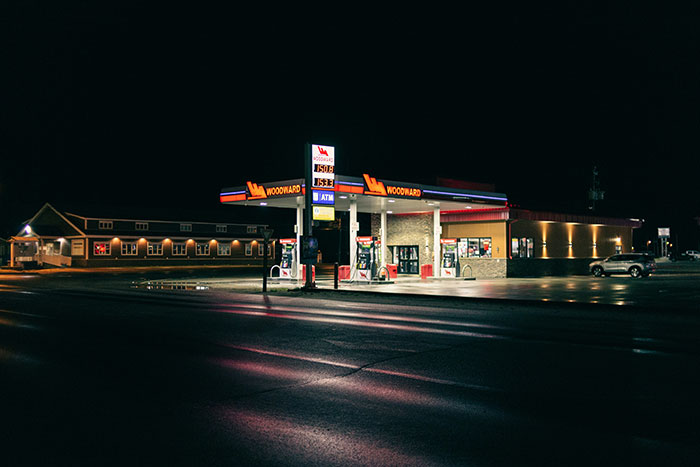 Gas station at night with illuminated pumps and building, illustrating gas station workers sharing wildest stories.