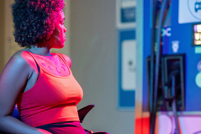 Woman wearing bright orange top standing near a gas pump at night, representing gas station workers sharing wild stories.