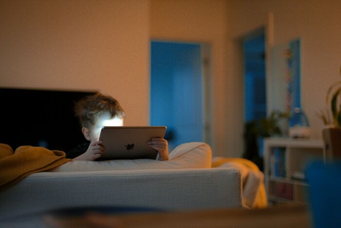 Child sitting on a couch using a tablet late at night, highlighting common parents fail at raising kids issues.