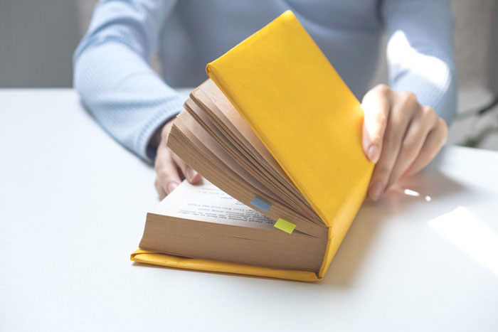 Person flipping through a yellow book carefully, symbolizing strict adherence to rules by the book in an office setting.