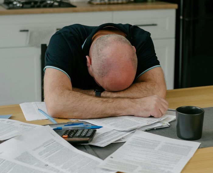 Man with head down overwhelmed by bills and calculator, symbolizing internet users’ concern about scams.