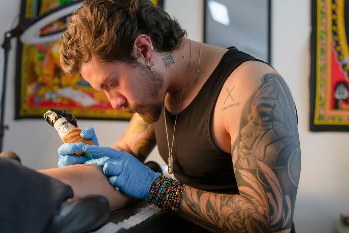 Tattoo artist with colorful bracelets and tattoos creating a detailed ink design, showcasing insider experiences of nepo babies.