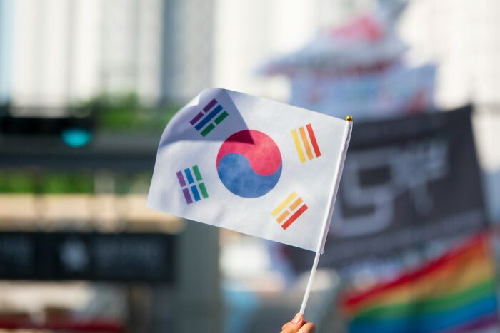 Hand holding South Korean flag outdoors with blurred city background representing smart man from South Korea seeking US asylum