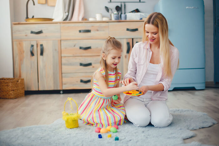 Woman and young child play on floor in kitchen, highlighting challenges of daily screaming and meltdowns with 3-year-old toddler.
