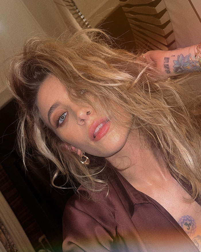 Paris Jackson with tousled hair and visible tattoos, sharing her experience of substance use deforming her face.