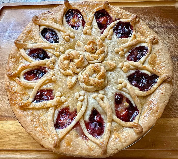 Round baked pie with decorative crust and fruit filling, showcasing gorgeous baked goods with artistic kitchen skills.