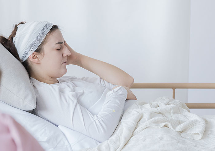 Young woman with head bandage resting in hospital bed, symbolizing coma survivors sharing their recovery stories.