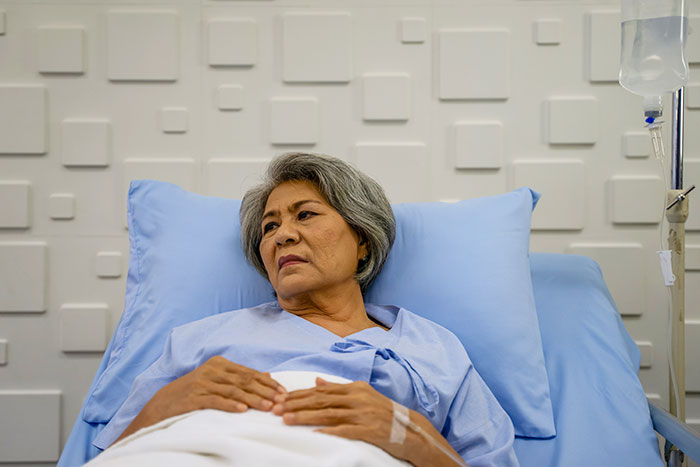 Elderly woman in hospital bed receiving IV treatment, reflecting on her experience as a coma survivor.