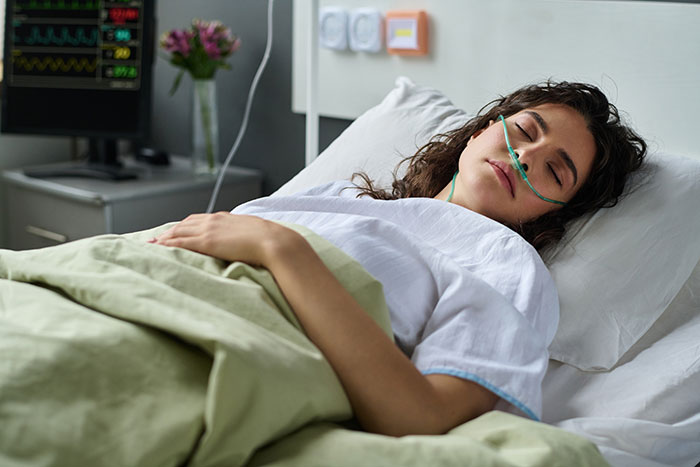Young woman in hospital bed with oxygen tube, appearing unconscious, representing coma survivors’ stories and experiences.