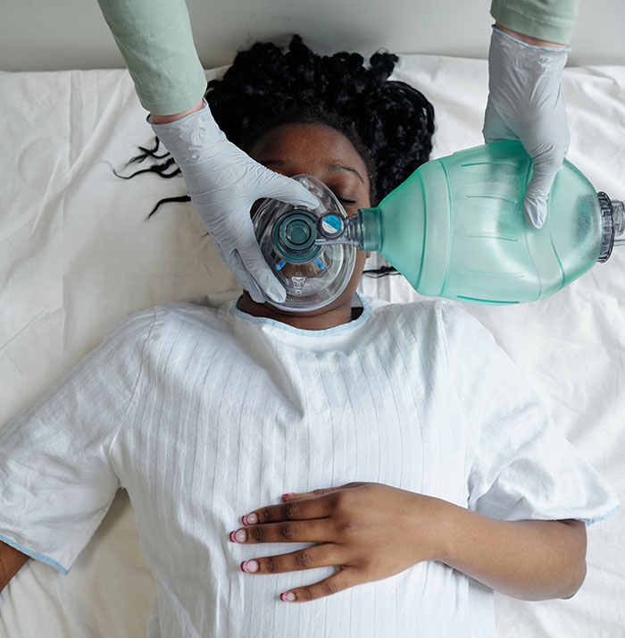Patient in coma receiving ventilation support from medical professional wearing gloves in a hospital setting.