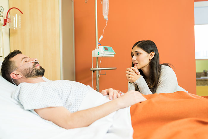 Man lying in hospital bed in a coma with woman sitting beside him, highlighting coma survivors' emotional stories.