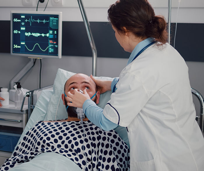Patient in hospital bed receiving care from nurse near heart monitor, highlighting coma survivor medical support and recovery.