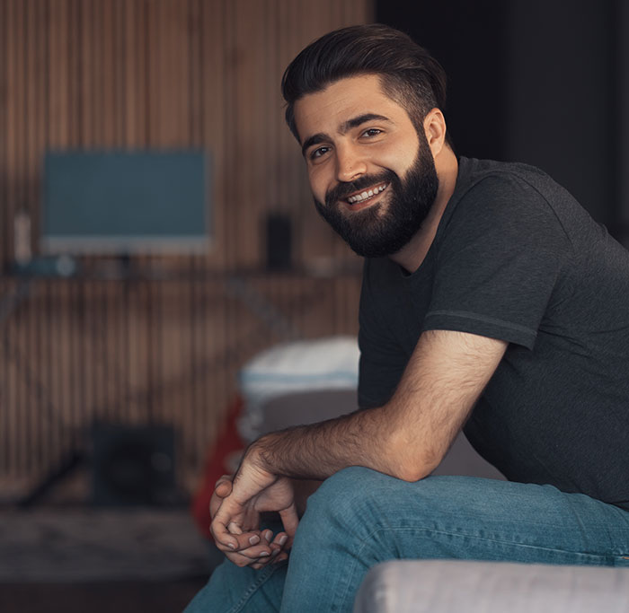 Young man with beard sitting and smiling indoors, representing people who walked away from old lives and started anew.
