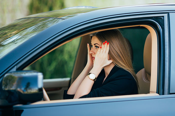 Young woman with red nails and wristwatch sitting in car, reflecting on walking away from old life and starting new one.