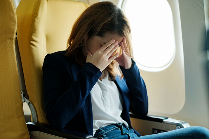 Woman feeling overwhelmed and stressed on an airplane, reflecting challenges of walking away from old lives and starting new ones