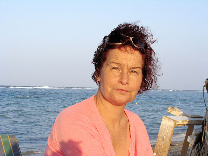 Woman with curly hair wearing a pink shirt by the ocean, representing people who walked away from their old lives.
