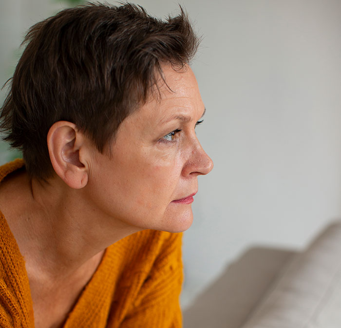 Middle-aged woman in an orange sweater looking thoughtfully, representing people who walked away from their old lives.