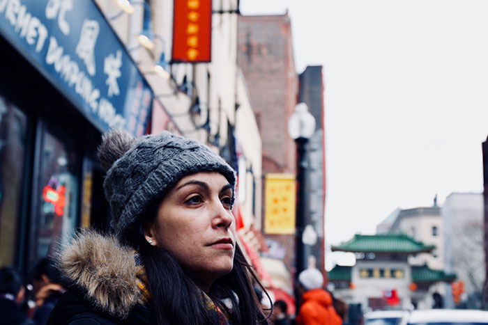 Woman wearing a knit hat and coat on a city street, representing people who walked away from old lives and started new ones.