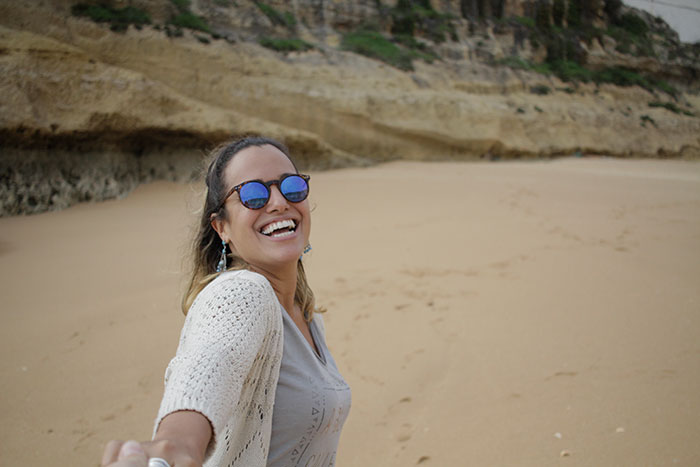 Smiling woman wearing sunglasses on a beach, symbolizing people who walked away from their old lives and started anew.