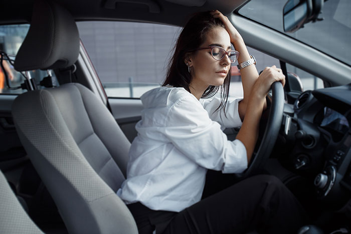 Woman sitting in a car looking reflective, symbolizing people who walked away from their old lives to start a new one.