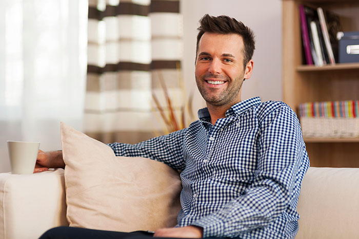 Smiling man sitting on a couch at home, representing people who walked away from their old lives and started new ones.