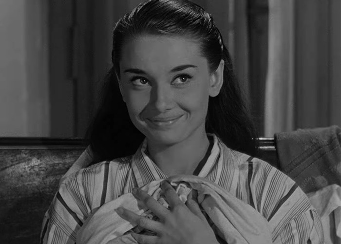 Black and white photo of Audrey Hepburn smiling gently while holding fabric, illustrating reactions to Audrey Hepburn actually aging.