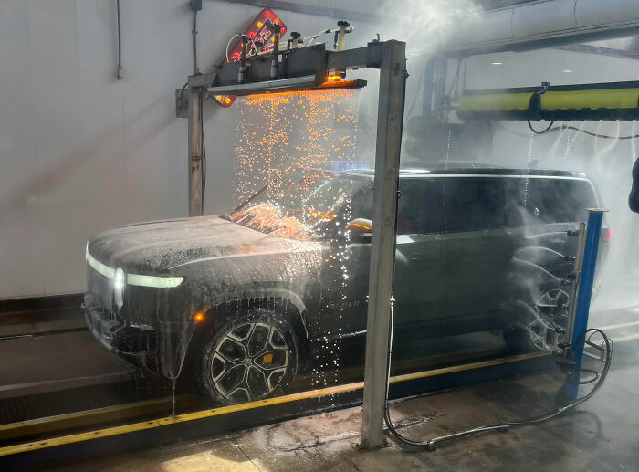 Electric SUV undergoing automated wash with sparks flying, illustrating a lucrative loophole exploited in car maintenance.