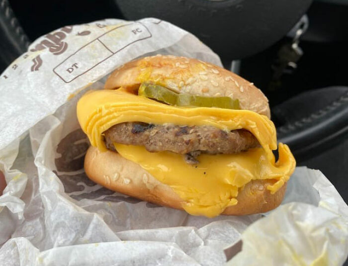 Burger with excessive melted cheese and pickles inside a sesame bun, showcasing a lucrative loophole food hack.