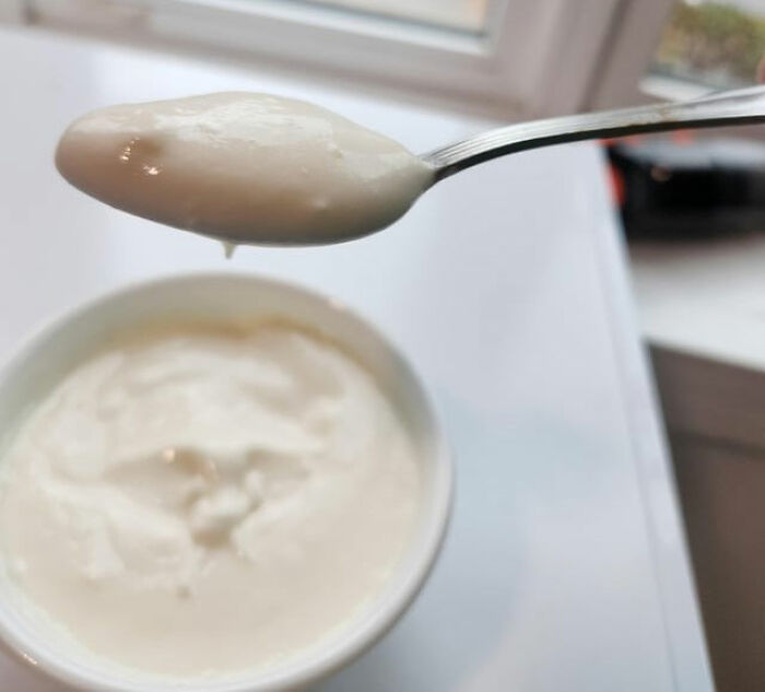 Close-up of creamy yogurt on a spoon above a white container showing kitchen tips and tricks to upgrade cooking skills.