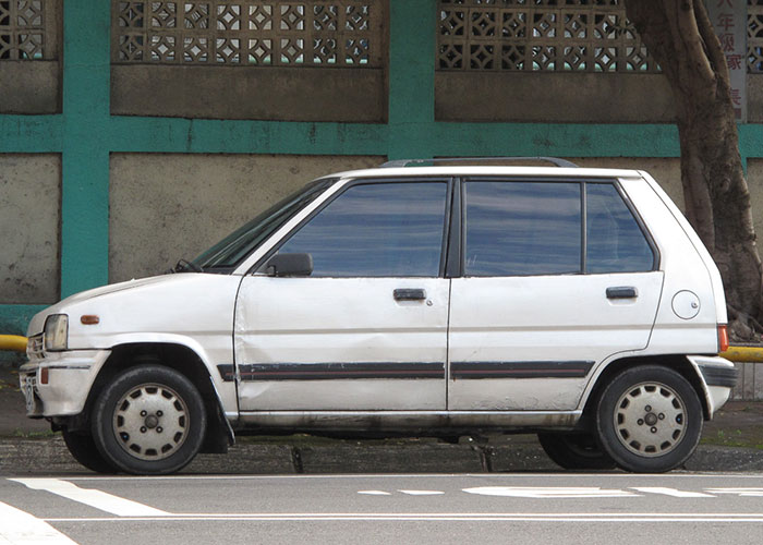Old white compact car parked on street, representing discontinued things and foods people are upset about.