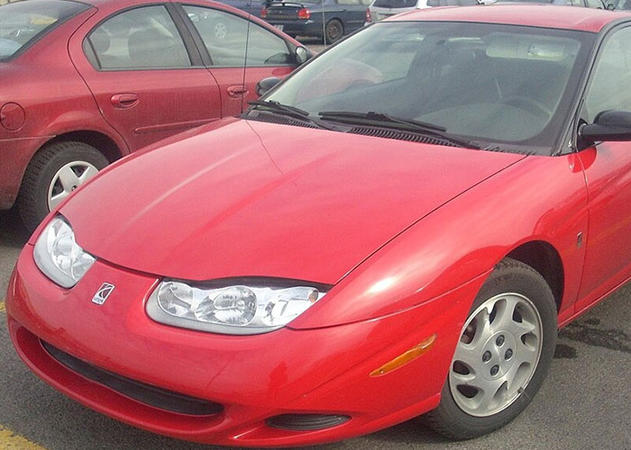 Red discontinued Saturn sports car parked in a lot with other vehicles, a nostalgic item people miss today