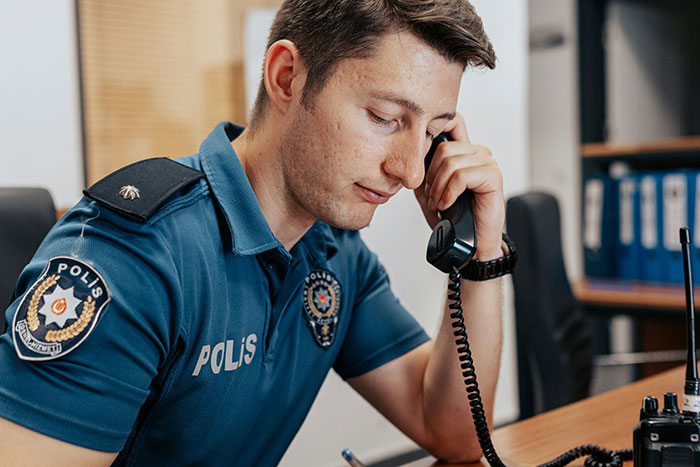 Police officer in uniform speaking on a landline phone, focused on a call in an office setting.