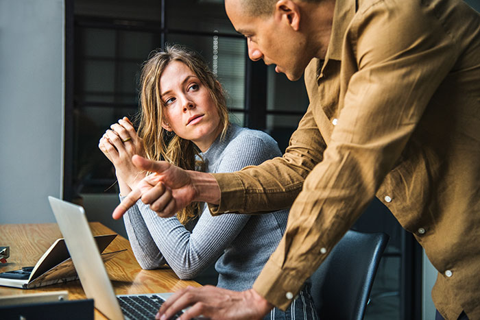 Woman refusing to return coworker&rsquo;s expensive jacket while having a tense conversation at office desk with laptop.