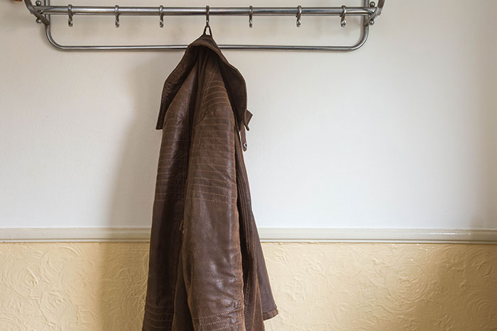 Brown leather jacket hanging on a metal rack against a plain wall, related to coworker refusing to return expensive jacket.
