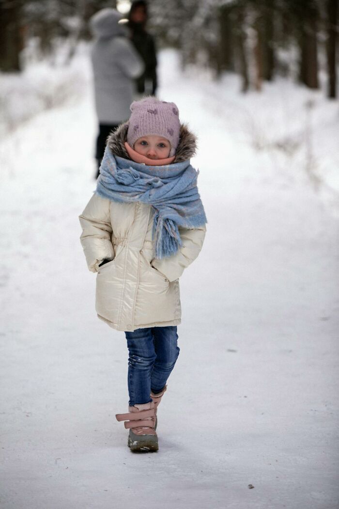 Young child bundled in winter clothing walking on snowy trail with park rangers in background, capturing creepy park ranger moments