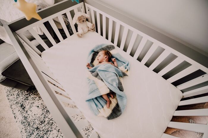 Baby wrapped in a blue blanket sleeping peacefully in a crib, capturing funny and serious moments parents face raising monsters.