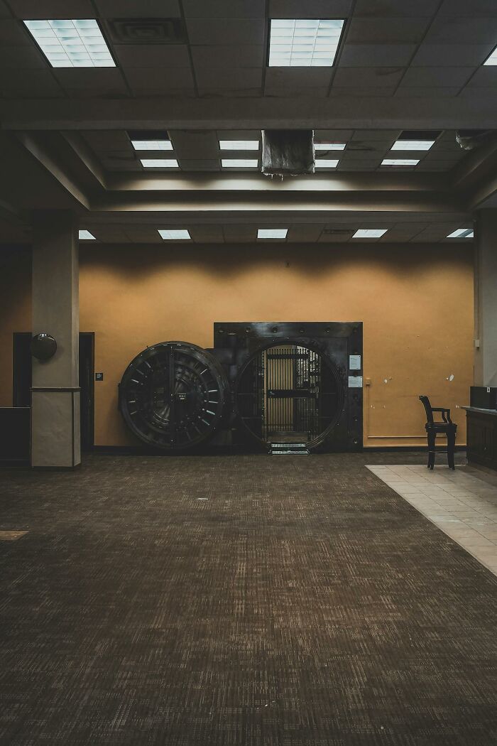 Abandoned bank vault with open steel door in a dimly lit room, capturing bizarre moments of eerie stillness.
