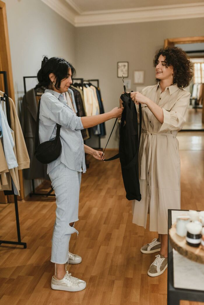 Two women shopping in a boutique, one showing clothing to the other in a casual, friendly environment, Karen examples concept.