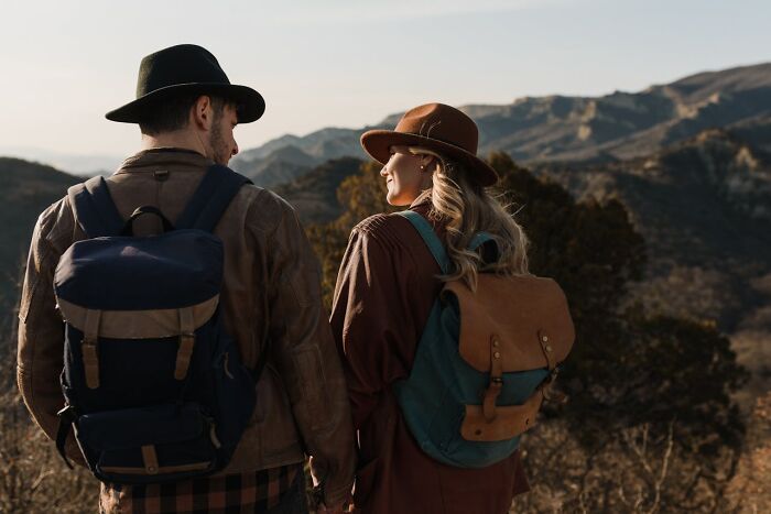 Two hikers wearing backpacks and hats overlooking mountainous wilderness, capturing creepy things witnessed by park rangers.