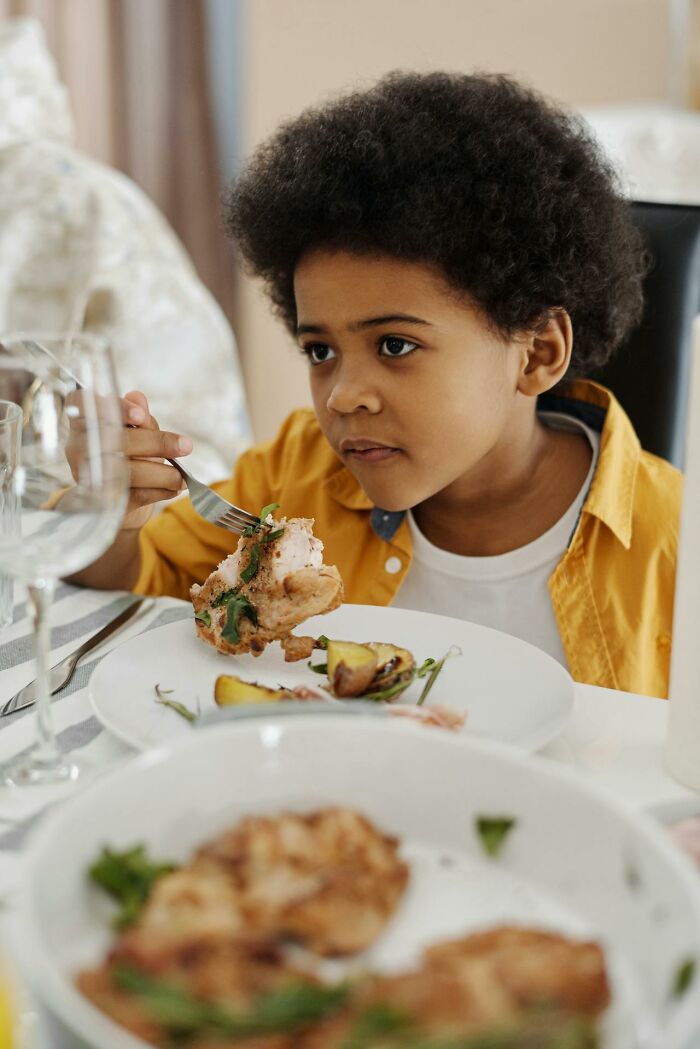 Child eating chicken with focused expression, illustrating childhood habits that seem unusual or not normal.